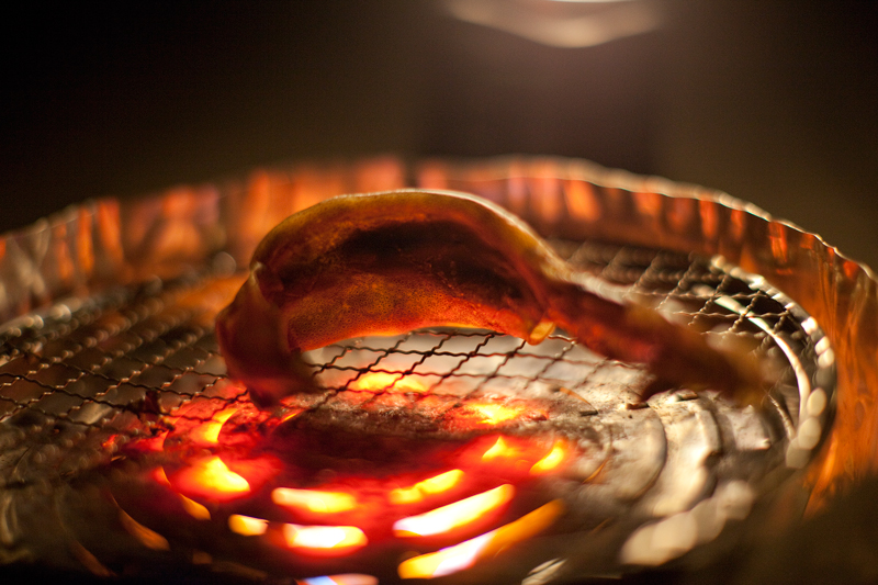 真っ赤に焼けた網の上で反る干しイカ